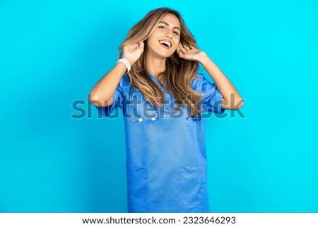young beautiful doctor woman standing over blue studio background Trying to hear both hands on ear gesture, curious for gossip. Hearing problem, deaf