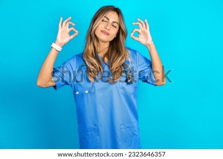young beautiful doctor woman standing over blue studio background relax and smiling with eyes closed doing meditation gesture with fingers. Yoga concept.