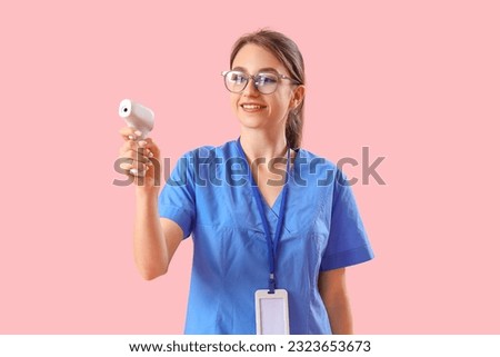 Female medical intern with infrared thermometer on pink background