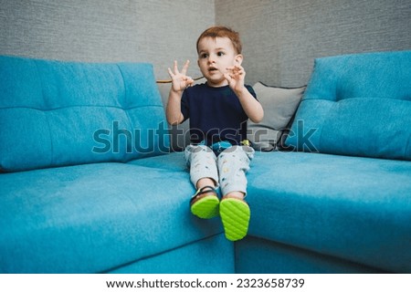 Two-year-old little boy sitting on the sofa at home, home entertainment of a small child.