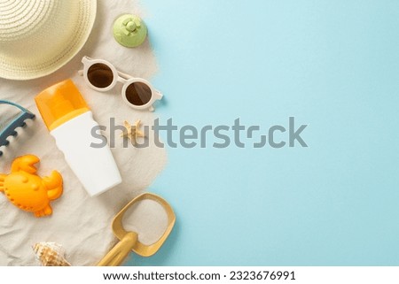 Beach activities for children concept. High angle view picture capturing sunhat, sunglasses and sunscreen bottle with sand molds and seashells on the sand on isolated blue backdrop offering copyspace