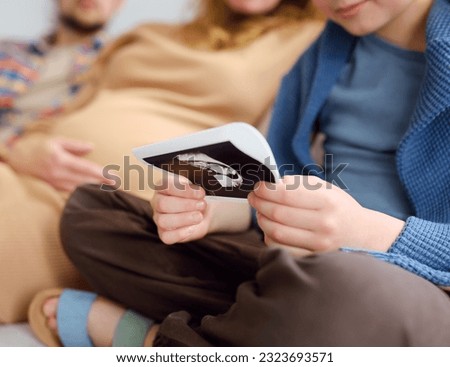 Parents inform his son that their family will soon have one more baby. Preteen boy will have brother or sister. Child is looking of ultrasound pictures of new baby. Relationships of siblings