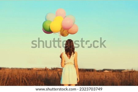 Rear view of young woman with bunch of colorful balloons in field outdoors on blue sky background