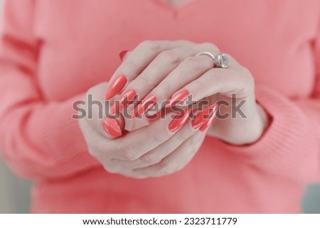 Woman hand with long nails and light orange coral neon manicure holds a bottle of nail polish
