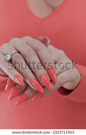 Woman hand with long nails and light orange coral neon manicure holds a bottle of nail polish
