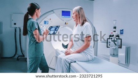 Male doctor and female patient are having talk at tomography chamber. African American doctor is holding tablet and showing MRI scans to patient. Doctor is satisfied with results and smiling. Royalty-Free Stock Photo #2323721295