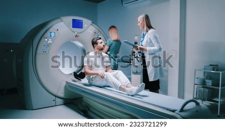 Male patient is waiting to be scanned. Man have talk with female doctor. Nurse is preparing for performing of magnetic resonance tomography. Patient is getting ready for MRI examining. Royalty-Free Stock Photo #2323721299