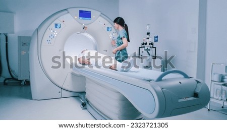 Patient is getting recommendations from doctor before MRI procedure. Woman is lying down at CT scanner bed. Female is moving into MRI scanner capsule. Female doctor is conducting tomography examining. Royalty-Free Stock Photo #2323721305