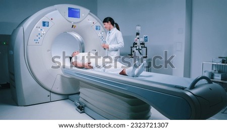 Female medical worker dressed up in gown before MRI examination. Female doctor is preparing patient for magnetic resonance procedure. Patient is lying at CT scanner bad and waiting to be scanned. Royalty-Free Stock Photo #2323721307