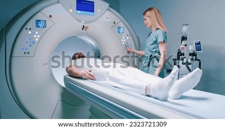 Patient is preparing for MRI examination. Man enters into MRI capsule. Female doctor calms patient and conducts magnetic resonance imaging. Medical worker is pressing buttons on MRI capsule.