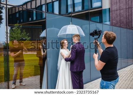 Professional wedding videographer shoots a movie with the newlyweds under an umbrella next to a glass wall