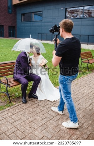 Professional wedding videographer shoots a film with the newlyweds on a bench under an umbrella