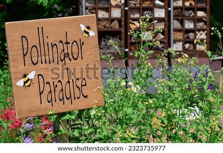 Pollinator Paradise sign in a garden with flowers and insect hotel in the background