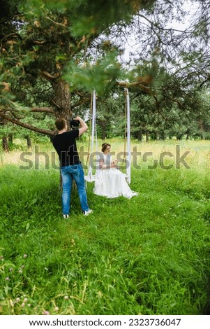 Professional wedding videographer shoots a film with a bride on a rope swing in a pine forest