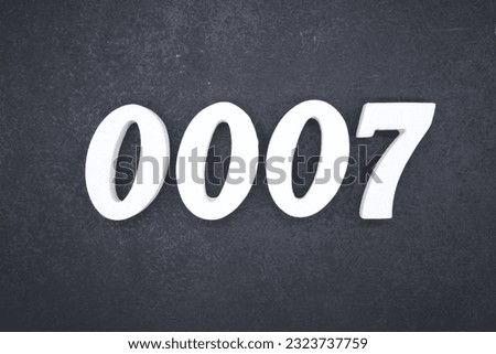 White number 0007 on plywood with black paint as background.