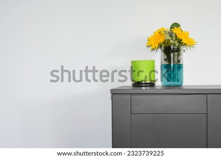 Interior decoration with a vase of sunflowers and a green candle sitting on a black cabinet