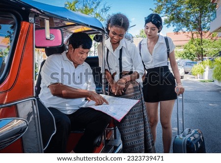 Young girl tourists with luggage discussing and bargaining tuktuk service with travel map by pointing on locations on map. Travel concept. Royalty-Free Stock Photo #2323739471