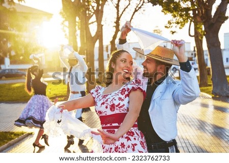 small group of Latin American young adults dressed as huaso dancing cueca in the town square at sunset Royalty-Free Stock Photo #2323762733