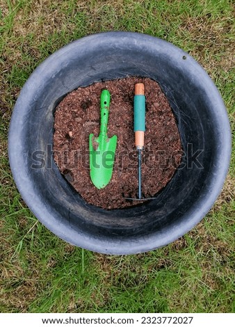 Green gardening tools are shovels and rakes placed in the soil pan. The background image is trees, leaves, lawns. Royalty-Free Stock Photo #2323772027