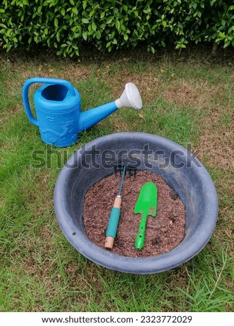 Green gardening tools are shovels and rakes placed in the soil pan. The background image is trees, leaves, lawns. Royalty-Free Stock Photo #2323772029