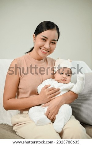 Young Adorable Asian mother holding her baby and sitting on the sofa in the living room. 
