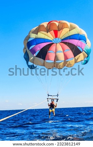 Parasailing water amusement - flying on a parachute behind a boat on a summer holiday by the sea. Summer vacation concept Royalty-Free Stock Photo #2323812149