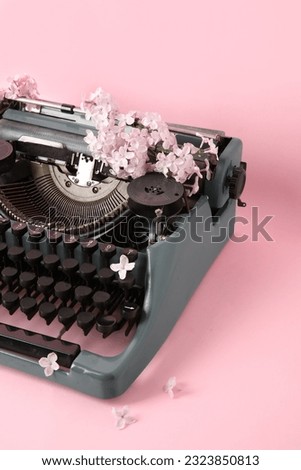 Vintage typewriter with lilac flowers on pink background, closeup