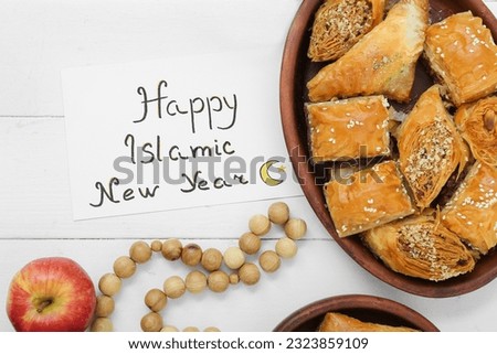 Card with text HAPPY ISLAMIC NEW YEAR, sweets and tasbih on light wooden background, closeup Royalty-Free Stock Photo #2323859109