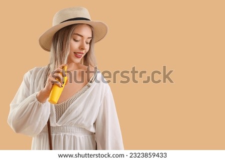 Young woman with sunscreen cream on beige background