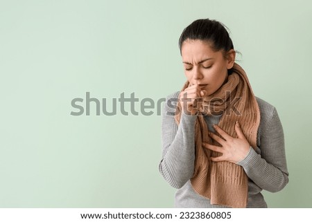 Ill young woman coughing on green background Royalty-Free Stock Photo #2323860805