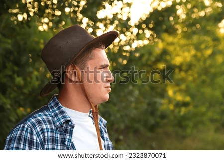 A young farmer in a cowboy hat stands proudly in an agricultural field, surrounded by the beauty of nature. With a closeup portrait capturing his determined expression hardworking rancher. Copy space