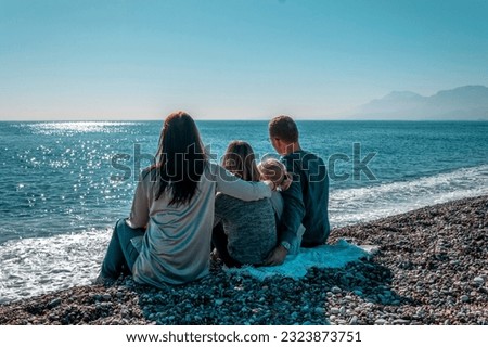 A family with children sits on the beach in winter and looks out to sea. Winter vacation.