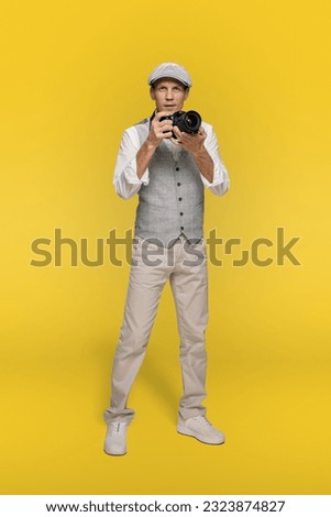 Smiling male photographer holding photo camera and taking pictures isolated on yellow background, creator with a beaming smile, embracing his passion for photography, seizing captivating shots