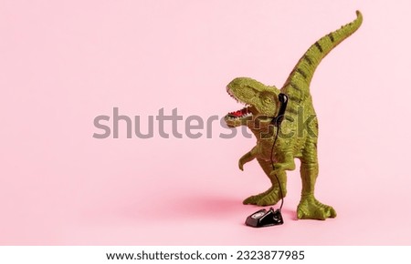 Cute green toy dinosaur speaking on retro phone on pink background. Copy space. 