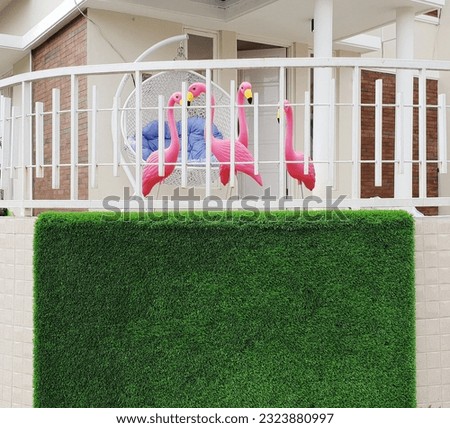 Exterior modern house street wall background with blank artificial green grass vertical decor. Mock up for signage template design. Front yard decor with pink flamingo statues and rattan swing. 
