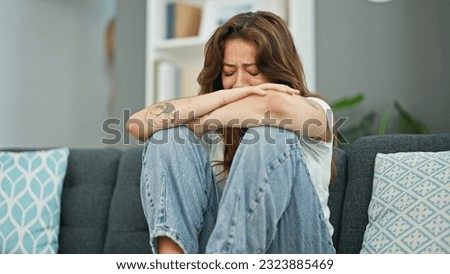 Young beautiful hispanic woman sitting on the sofa crying at home Royalty-Free Stock Photo #2323885469