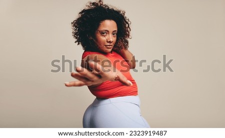 Woman looking at the camera as she moves her body in sportswear. Embracing her physique, she shows confidence and self-assurance in a studio. Female expressing herself through graceful body movements. Royalty-Free Stock Photo #2323919487