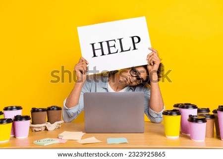 Portrait of unsatisfied tired guy hands hold help banner desktop workplace netbook coffee cup isolated on yellow color background Royalty-Free Stock Photo #2323925865