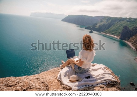 Freelance woman working on a laptop by the sea, typing away on the keyboard while enjoying the beautiful view, highlighting the idea of remote work. Royalty-Free Stock Photo #2323940303