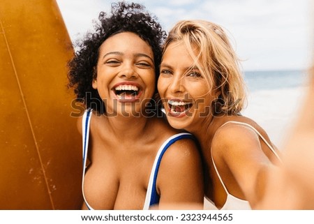 Happy female friends having a fun surfing adventure together on a carefree summer vacation. Two young women enjoying beach activities, surfing, and capturing memories together.