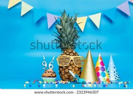 Creative background with pineapple character in sunglasses copy space. Happy birthday background with muffin or cake with candle number  96. Anniversary holiday decorations on a blue background.