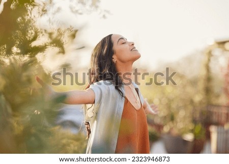 Young latin woman with arms outstretched breathing in fresh air during sunrise at the balcony. Girl enjoying nature while meditating during morning with open arms and closed eyes. Mindful woman relax. Royalty-Free Stock Photo #2323946873
