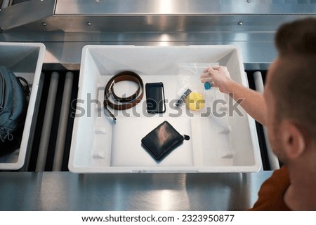 Airport security check before flight. Passenger holding plastic bag with liquids above container with personal items. 
 Royalty-Free Stock Photo #2323950877