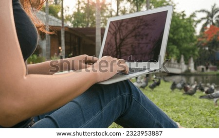 Woman sitting in park on the green grass with laptop, student studying outdoors. Copy space