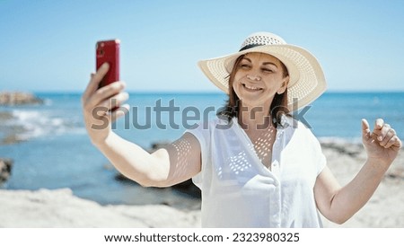 Middle age hispanic woman tourist smiling confident make selfie with smartphone at the beach