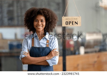 Successful african american woman in apron standing coffee shop door. Happy small business owner. Smiling portrait of entrepreneur standing with copy space. Royalty-Free Stock Photo #2323981741