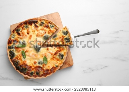 Delicious homemade salmon quiche with broccoli and spatula on white marble table, top view. Space for text