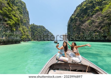 Asian woman friend using mobile phone taking selfie together during travel on boat passing tropical island beach lagoon in sunny day. Attractive girl enjoy outdoor lifestyle on summer holiday vacation