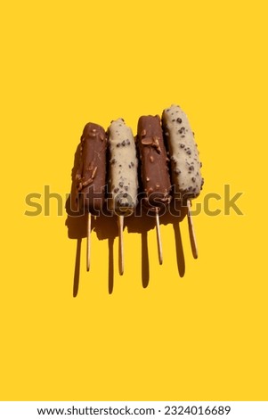 ice cream on a stick in white chocolate with cookies and milk chocolate with nuts on a yellow background