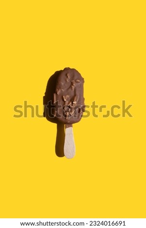 ice cream on a stick in white chocolate with cookies and milk chocolate with nuts on a yellow background